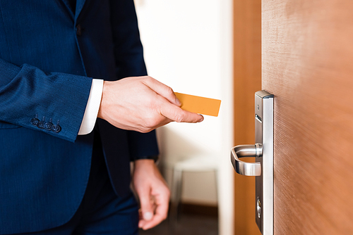 cropped view of businessman holding hotel card while standing near door