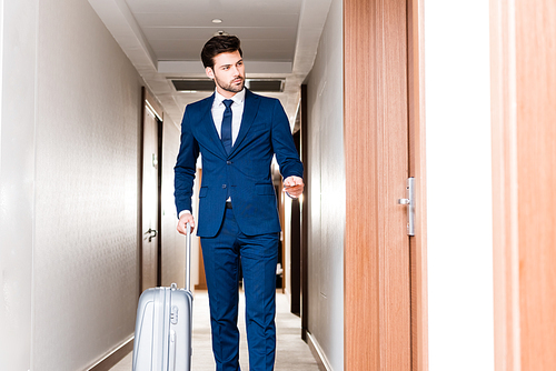 handsome man standing with luggage and holding hotel card in hotel corridor