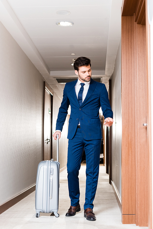 handsome businessman holding hotel card while standing with suitcase