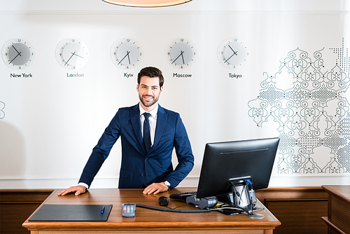 cheerful receptionist in suit standing near computer monitor in hotel