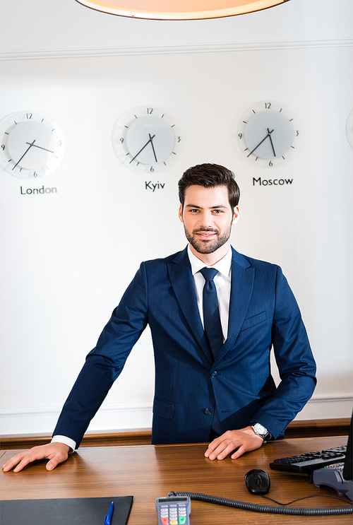 cheerful bearded receptionist standing at reception desk in hotel