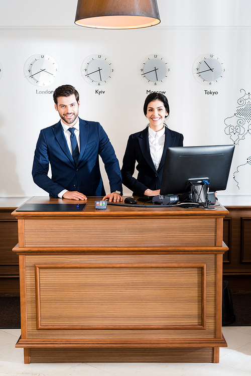 cheerful receptionists in formal wear standing at reception desk