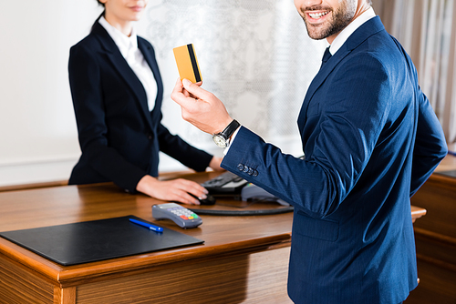 cropped view of cheerful businessman holding credit card near receptionist