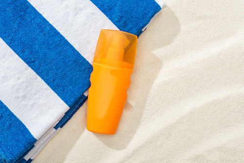 orange bottle of sunscreen on sand with striped towel
