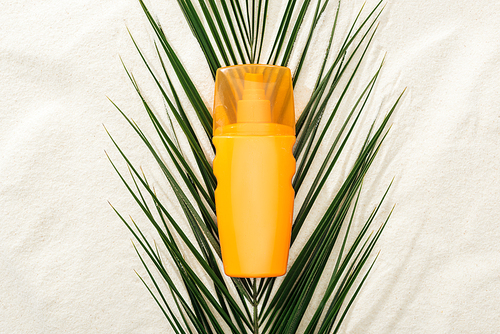 orange sunscreen lotion on green palm leaf on sand