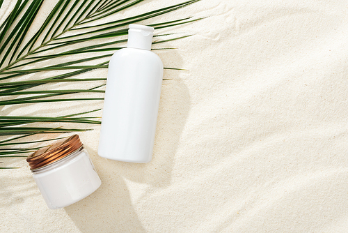 white sunscreen lotion and cream near green palm leaf on sand
