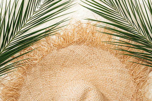 top view of stylish straw hat on golden sand with green palm leaves