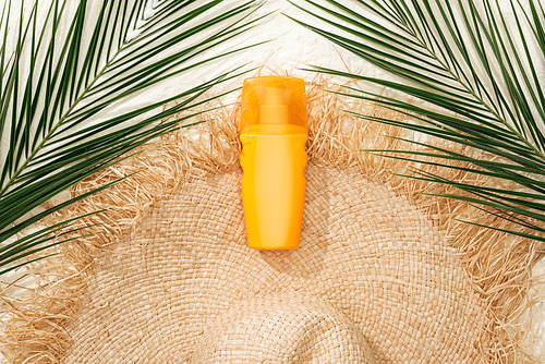 top view of stylish straw hat on golden sand with green palm leaves and sunscreen