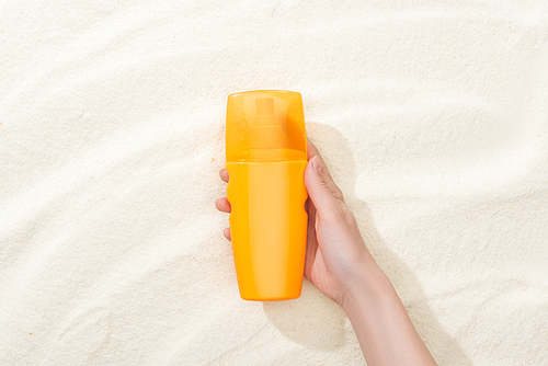 cropped view of woman holding orange sunscreen above golden sand