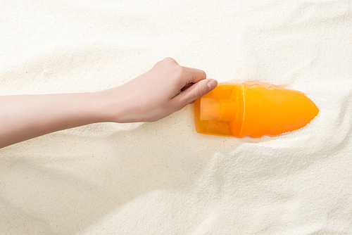 partial view of woman holding orange sunscreen above golden sand