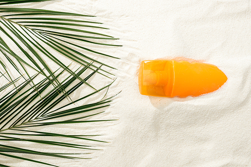 top view of sunscreen and green palm leaves on golden sand