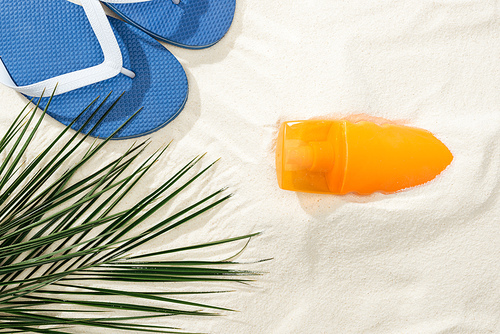 top view of sunscreen, palm leaf and flip flops on golden sand