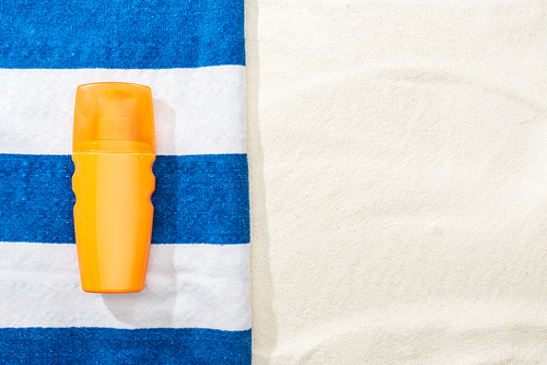 top view of sunscreen and striped blue and white towel on sand