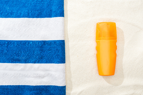 top view of sunscreen and striped blue and white towel on golden sand