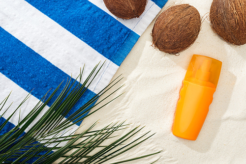 top view of palm leaves, coconuts and striped towel near orange sunscreen on sand