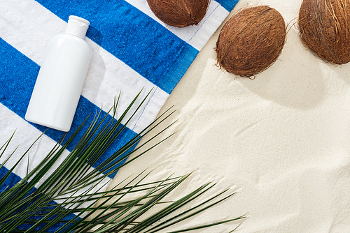 top view of palm leaves, coconuts and striped towel with white sunscreen on sand