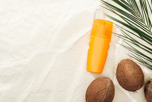 top view of palm leaf, coconuts and orange sunscreen on sand