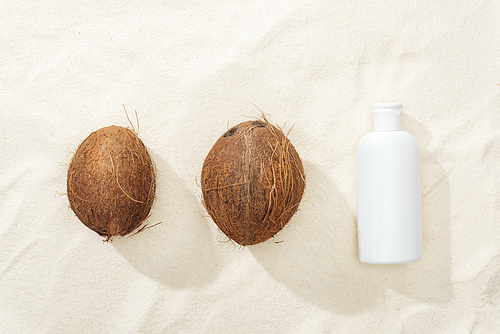 flat lay with white sunscreen lotion and coconuts on golden sand