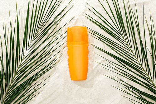 top view of palm leaves and orange sunscreen on sand
