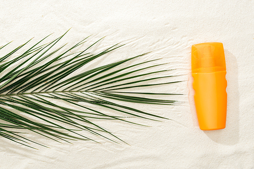 top view of palm leaf and orange sunscreen spray on sand