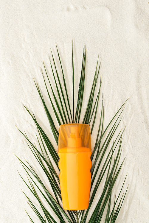 top view of palm leaf and orange sunscreen on sand
