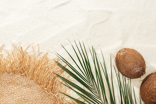 top view of palm leaf, coconuts and straw hat on sand