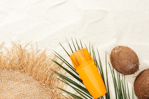 top view of palm leaf, orange sunscreen, coconuts and straw hat on sand