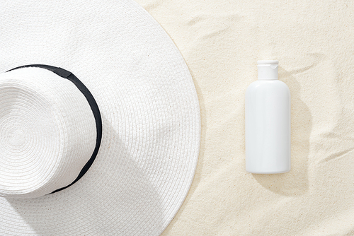 top view of white sunscreen lotion and straw hat on sand
