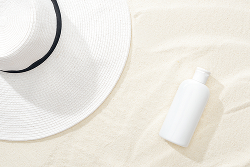 top view of white sunscreen and straw hat on sand
