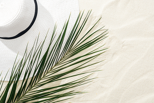 top view of white straw hat and green palm leaf on sand