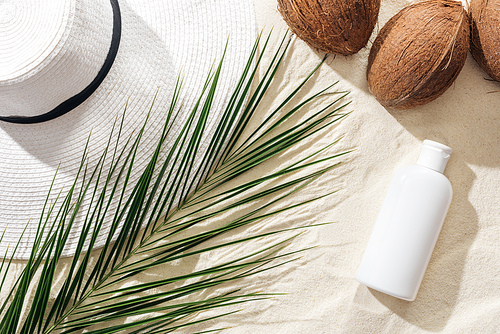 top view of palm leaf, sunscreen, coconuts and white straw hat on sand