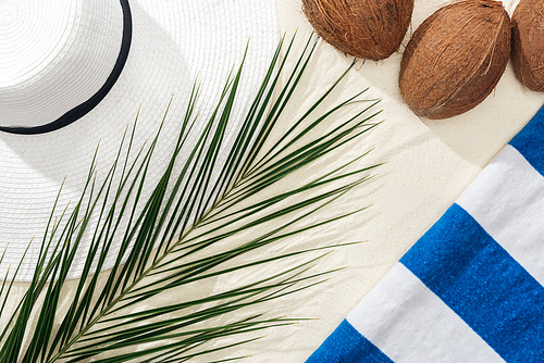 top view of palm leaf, striped towel, coconuts and white straw hat on sand