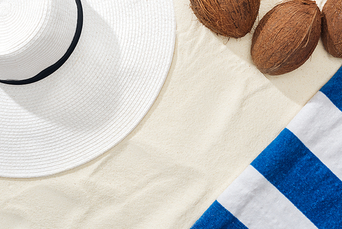 top view of coconuts, striped towel and white straw hat on sand