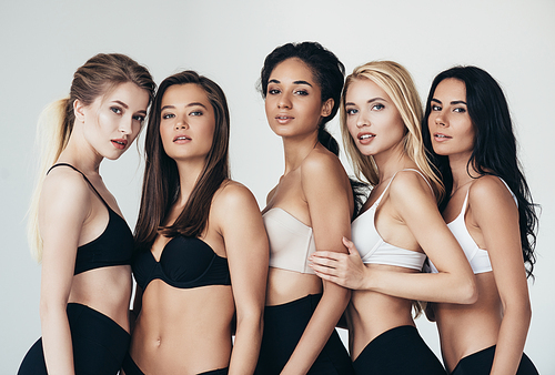five sexy multiethnic young women in underwear embracing isolated on grey