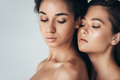 two attractive multiethnic young women with closed eyes isolated on grey