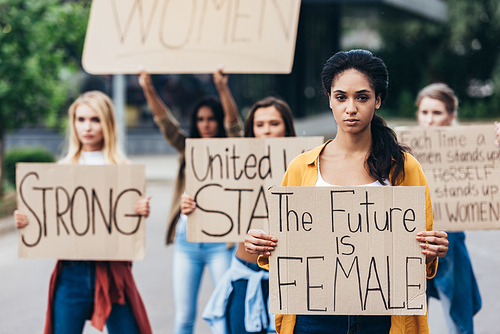 serious african american feminist holding placard with inscription the future is female near women on street