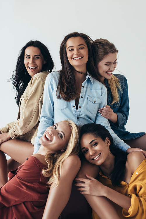 front view of five smiling attractive multiethnic feminists in colorful shirts embracing and  isolated on grey