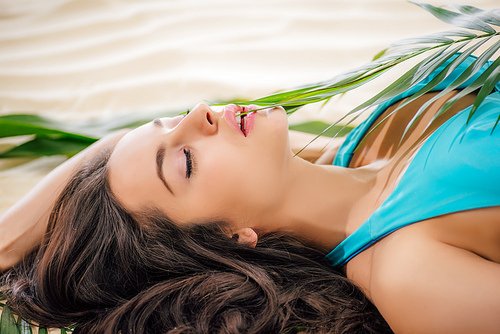 beautiful woman posing with green leaf and lying on beach with eyes closed