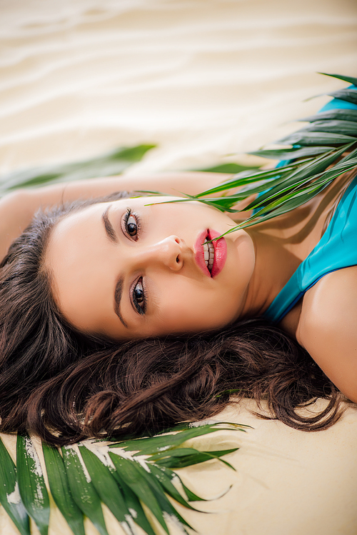 beautiful woman posing with green leaves and  while lying on beach