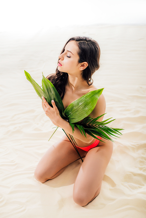 beautiful sexy woman covering breasts with leaves and posing on beach