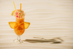 orange cocktail with sunglasses and cocktail umbrella on sandy beach with copy space