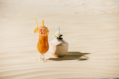 cocktail in coconut with flower and cocktail in glass on sandy beach