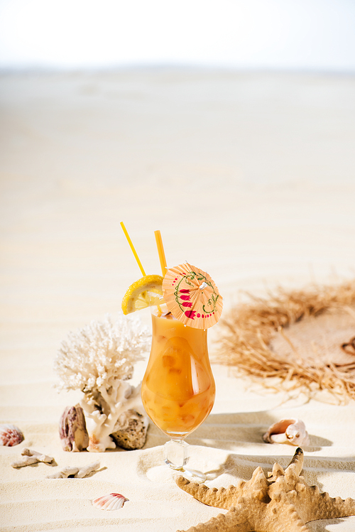 cocktail, starfish, coral and sea stones on sandy beach with copy space