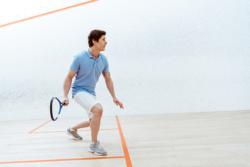Concentrated sportsman in blue polo shirt playing squash in sports center