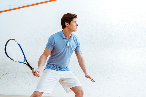 Concentrated sportsman in blue polo shirt playing squash in sports center
