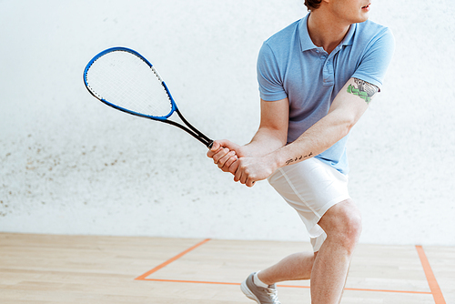 Cropped view of sportsman in blue polo shirt playing squash in sports center
