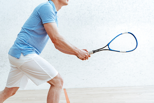 Cropped view of sportsman in blue polo shirt playing squash in sports center