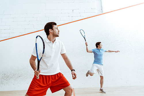 Two sportsmen playing squash with rackets in four-walled court