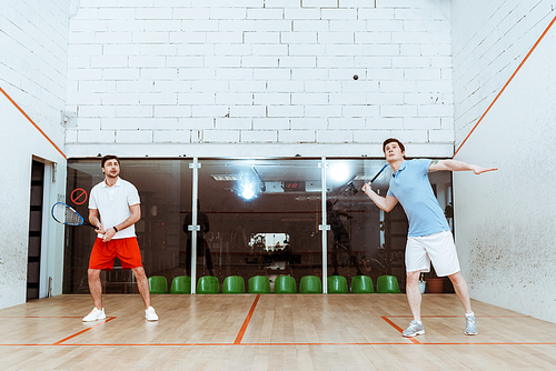 Full length view of two sportsmen playing squash with rackets in four-walled court