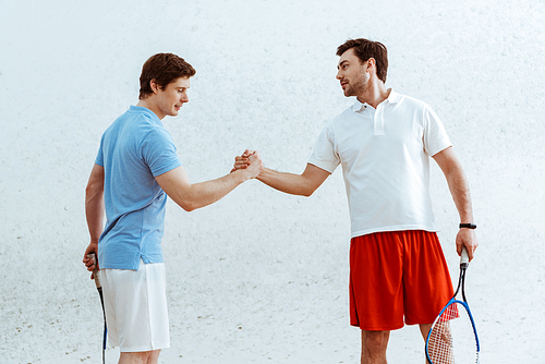 Two squash players with rackets shaking hands and looking at each other